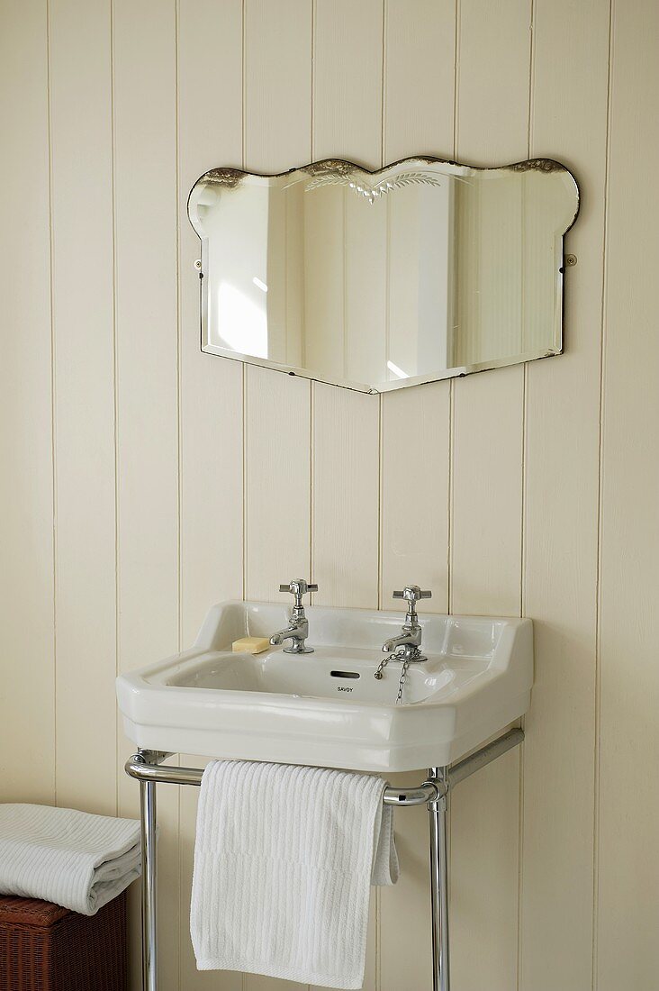 A wash basin with a chrome towel rail and a mirror on white wood panelling