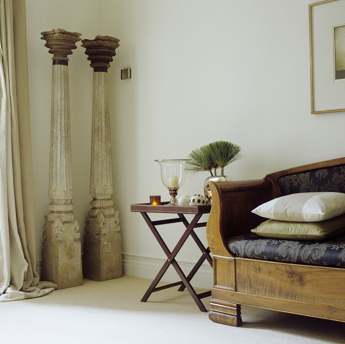 A delicate side table next to a wooden bench and decorative, antique pillars in a corner of a living room