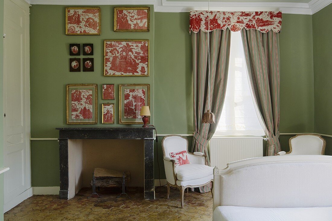 A bedroom with a fireplace and frame pieces of floral fabric on a green wall