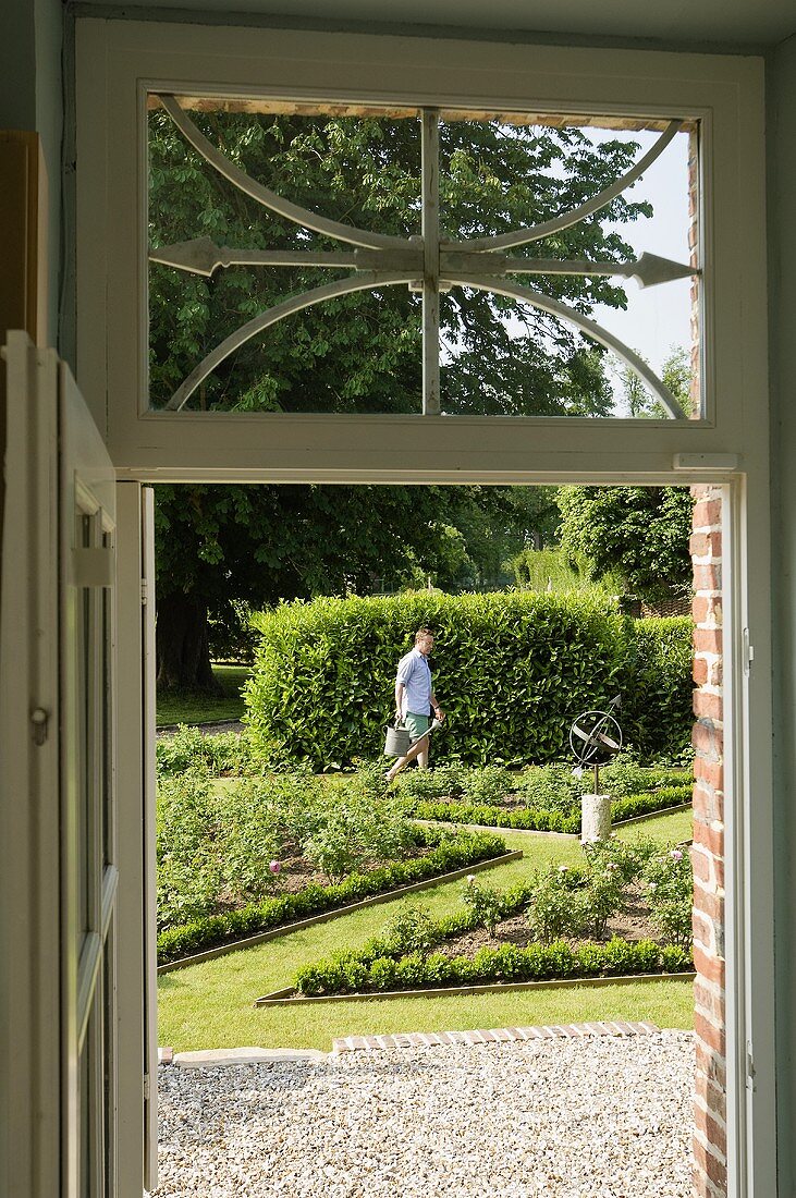 Blick durch die Tür in den Garten, Gärtner pflegt angelegte Rabatten