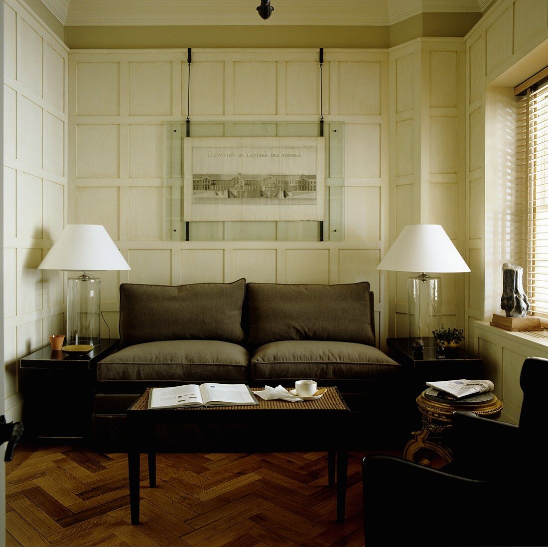 A brown two-seater sofa and table lamps in front of a white wood panelled wall