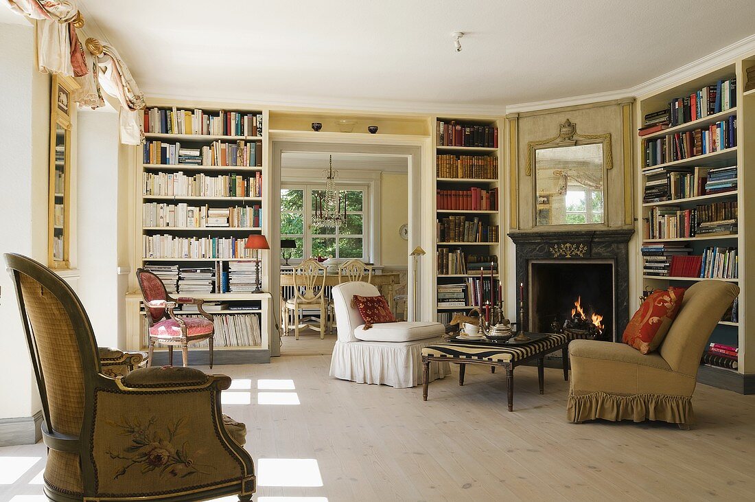 Upholstered armchairs in front of a fireplace in a living room-cum-library in a country house