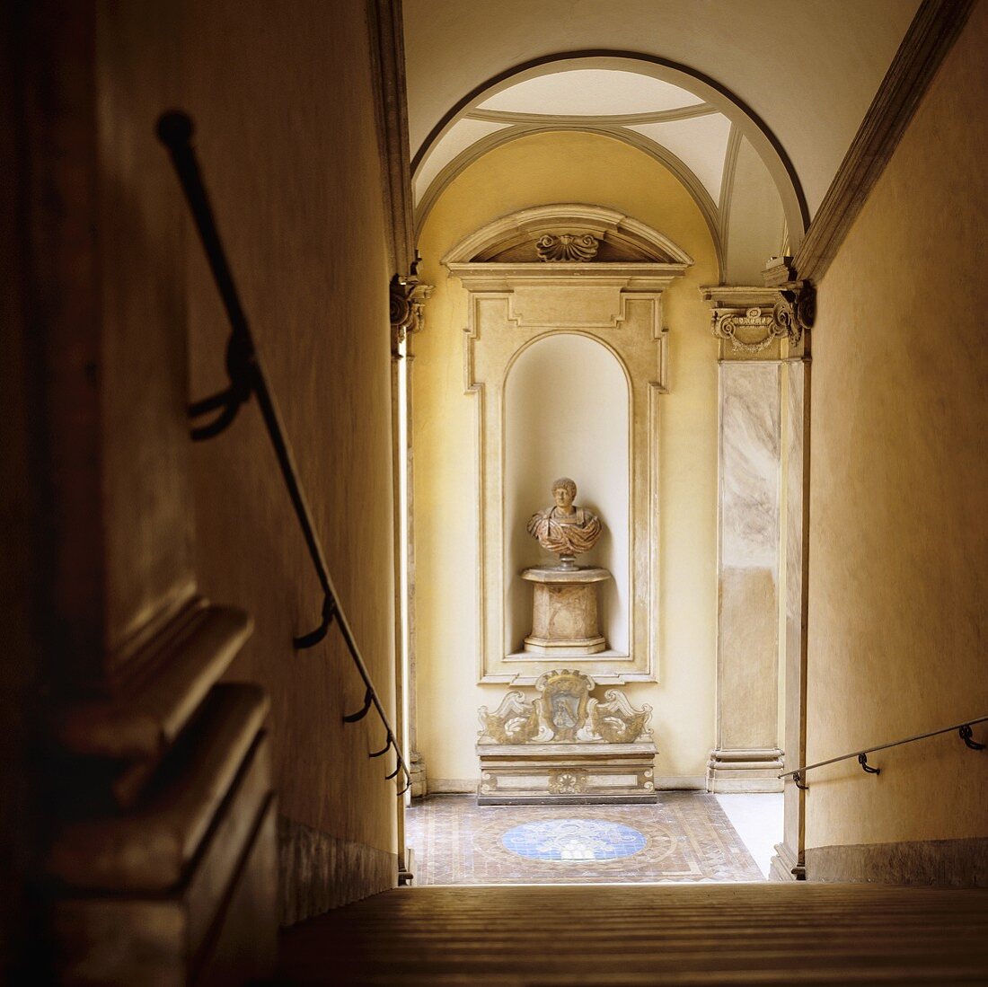 A stairway in a palazzo - a view from the stairs of a bust on a pedestal in a wall niche