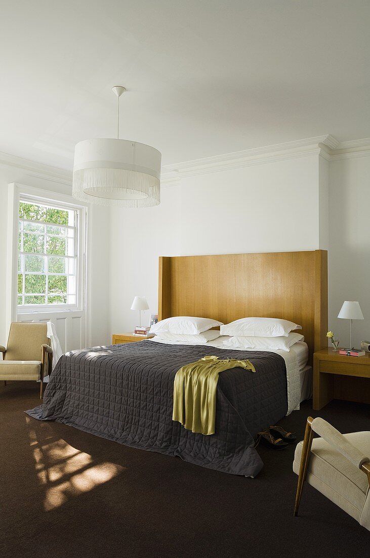 A bedroom with shades of brown and a bed with a high, wooden headrest