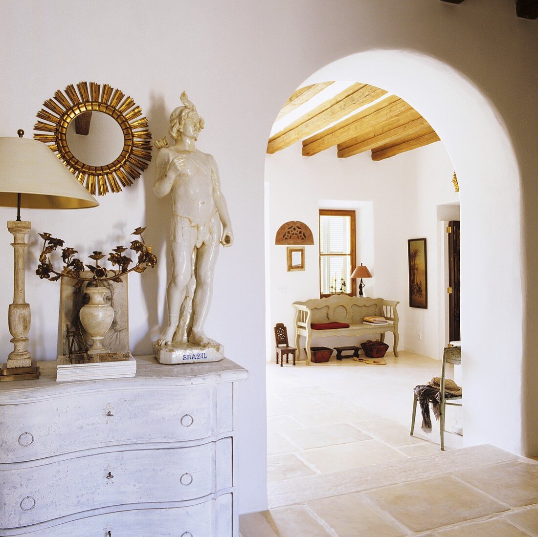 Antiques on a chest of drawers with a view through an arched doorway of a Mediterranean house