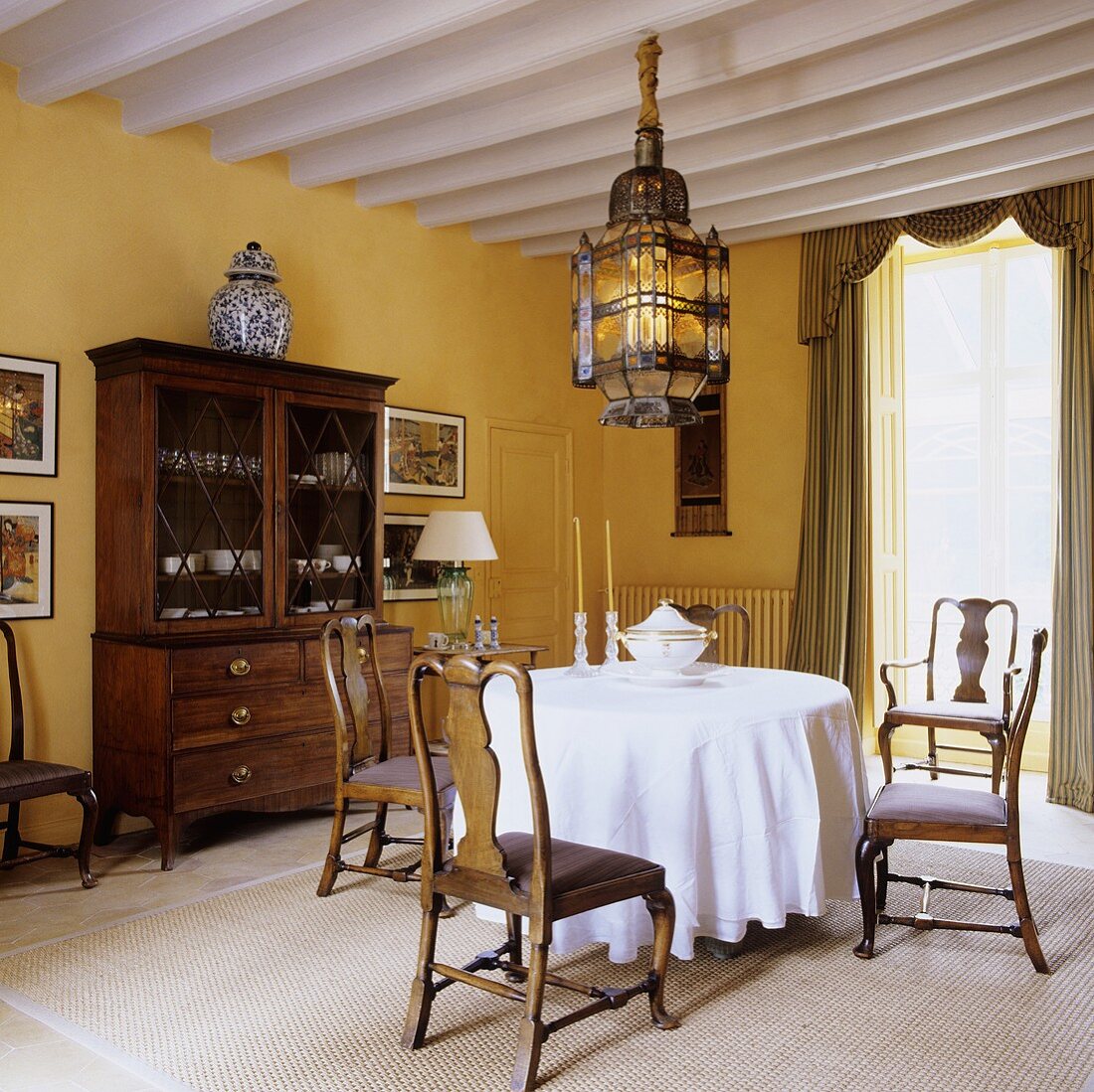 Antike Landhausmöbel mit orientalischer Deckenlampe im gelb getönten Esszimmer