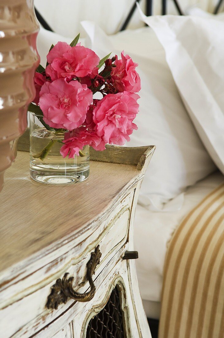 Pink flowers in a glass on an old fashioned bedside table