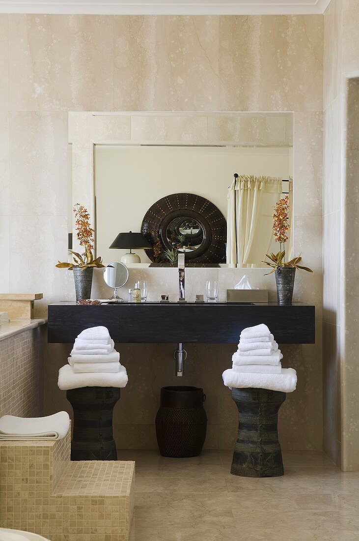 Stacks of towels on stools in front of a dark wooden washstand with a mirror