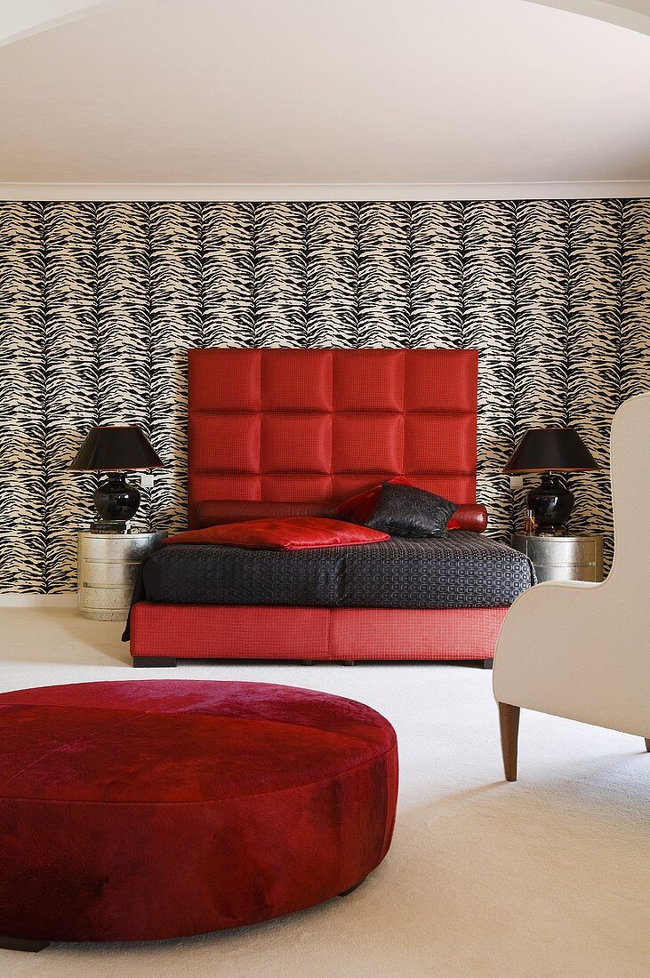 Peppiger Schlafraum - roter Sitzhocker vor rotem Bett mit gepolstertem Kopfteil an schwarzweisser Wand