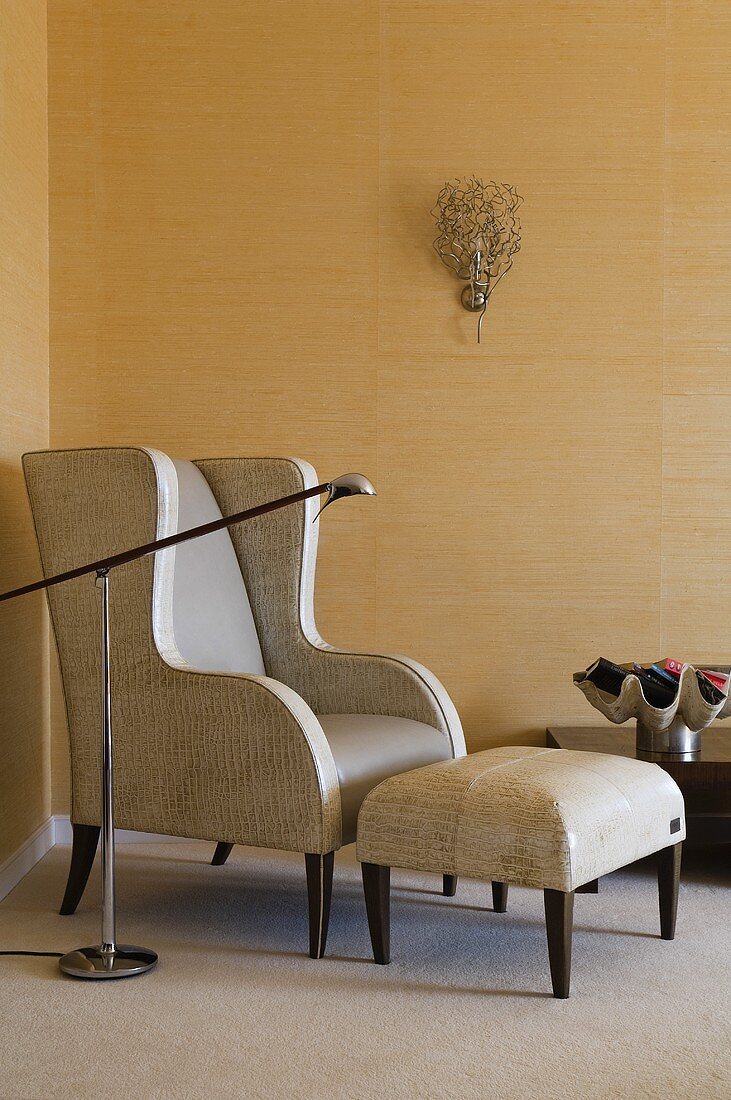 A leather armchair with a footstool and a floor lamp against a gold-papered wall in the corner of a room