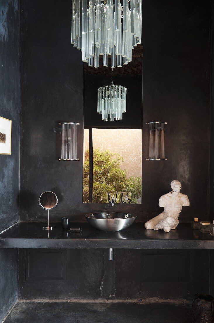 A dark grey concrete bathroom with a stone washstand, a stainless steel basin and a chandelier