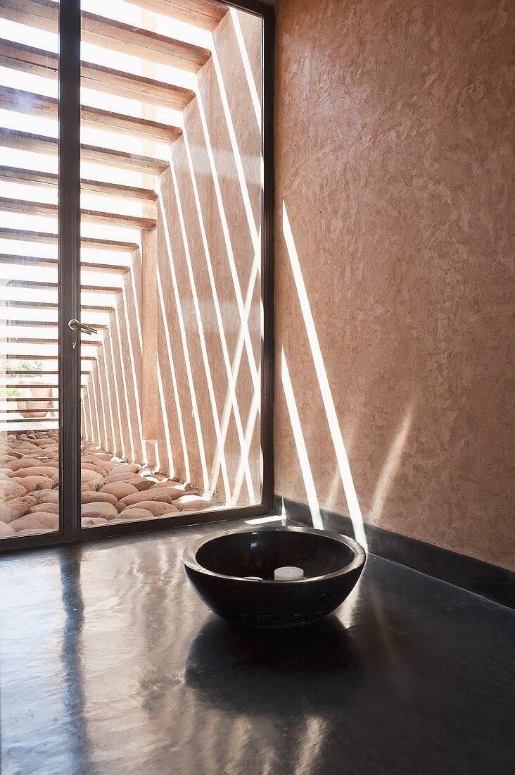 A wooden bowl in the hallway in front of a glass door with light playing over the wall and floor