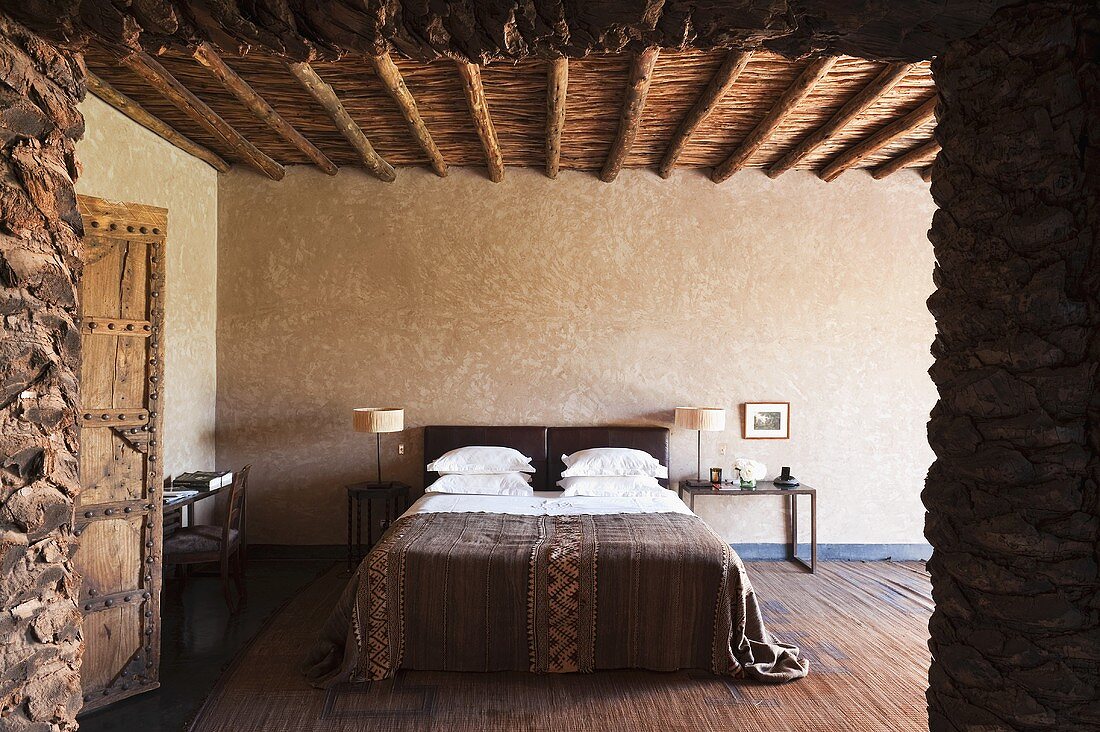 Blick auf Doppelbett im minimalistischen Schlafraum mit Holzbalkendecke im Mediterraner Landhaus