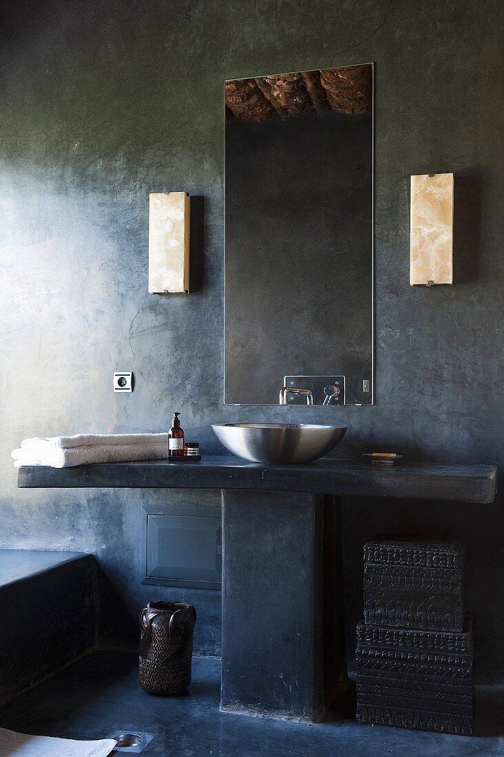 A concrete designer bathroom with a stone washstand with a stainless steel basin and a mirror