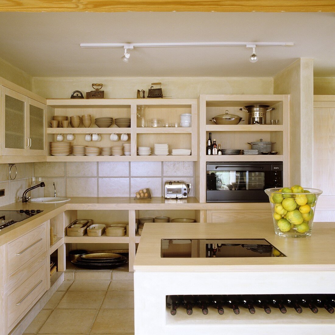 An open-plan kitchen featuring an island counter with a mini wine storage in front of stone shelves