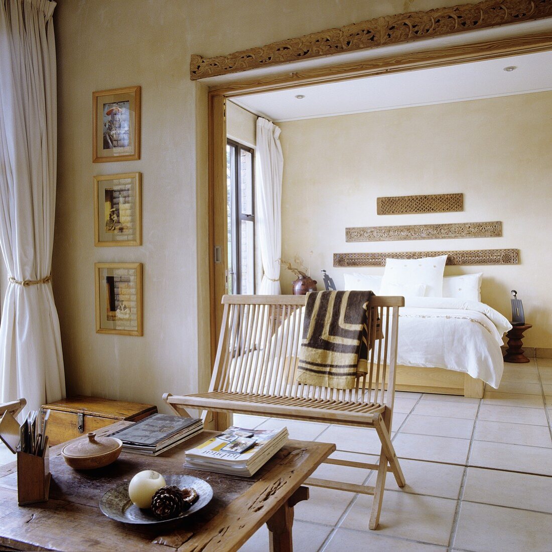 A table and a bench in front of a doorway leading to an open-plan bedroom