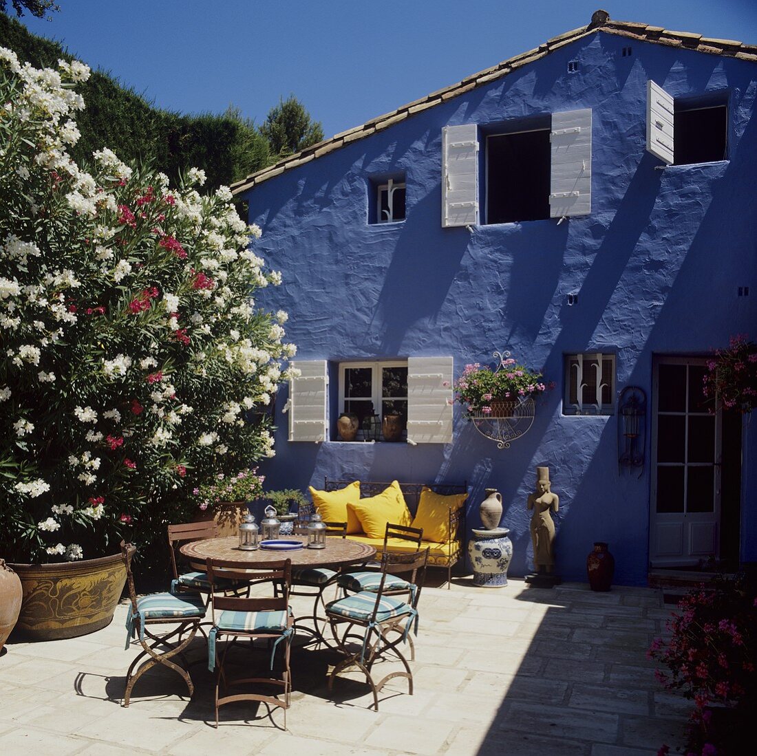 Holiday in a blue house - terrace tables and chairs in the sun next to scented oleanders