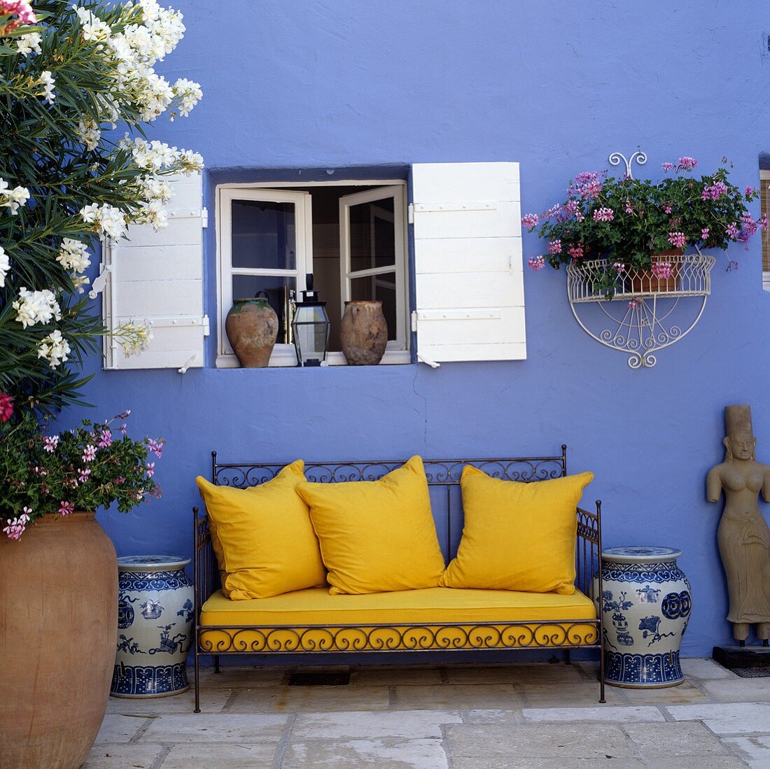 Gelbe Sofakissen auf verziertem Metallgestell vor blauer Hauswand