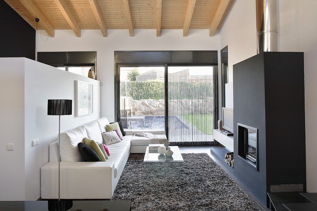 Designer-Wohnzimmer mit Gartenblick - Ledersofa vor Raumteiler gegenüber schwarzem Kaminofen