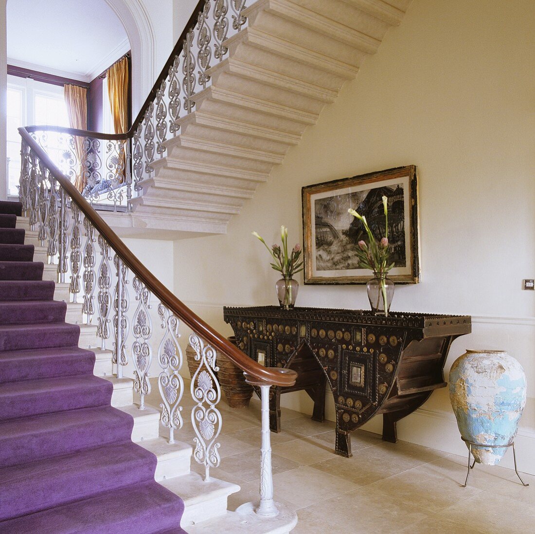 Eleganter Treppenaufgang mit Kunstschmiedegeländer und antikem Wandtisch in der Nische