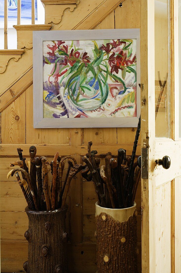 Pots of walking sticks and a picture in a hallway with a rustic wooden stairway