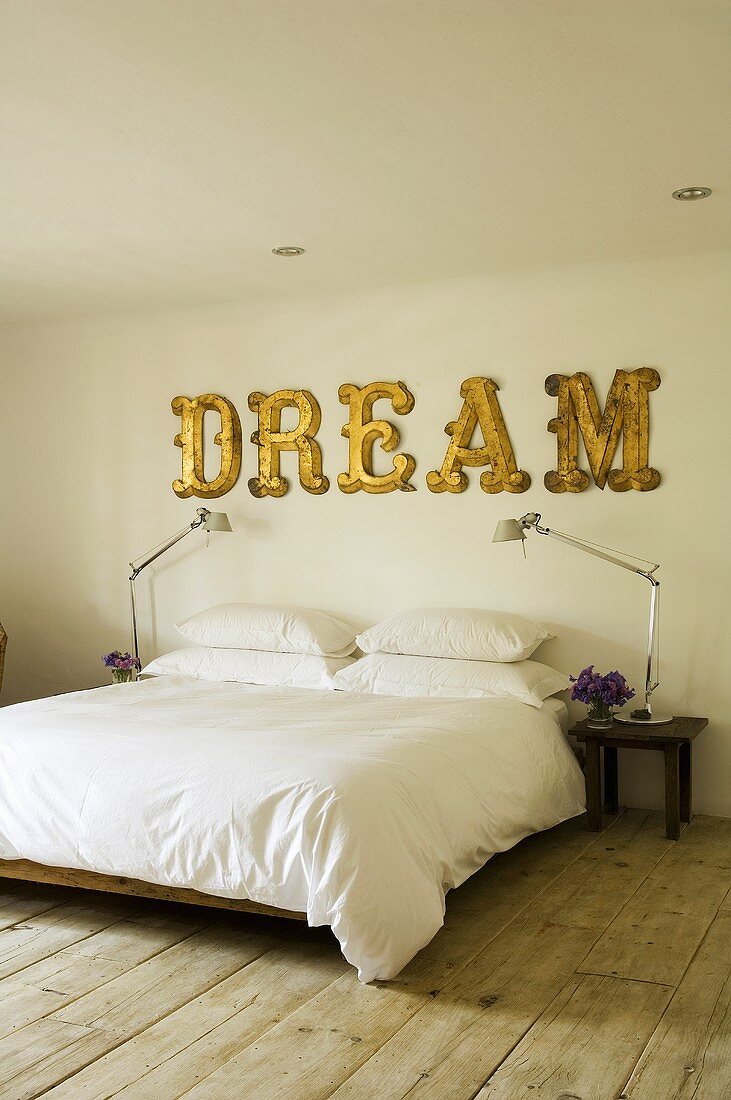 Bett mit weißem Bezug und englischer Schriftzug auf der Wand