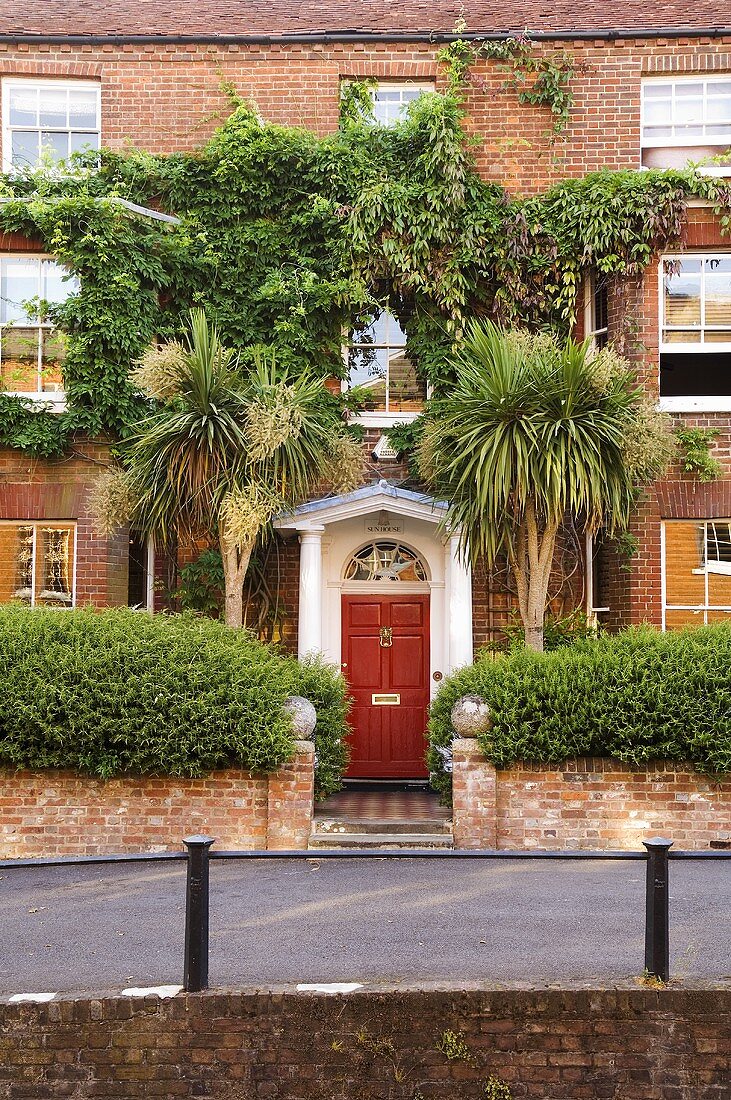 Englisches Stadthaus mit roter Eingangstür und Palmen vor Ziegelfassade