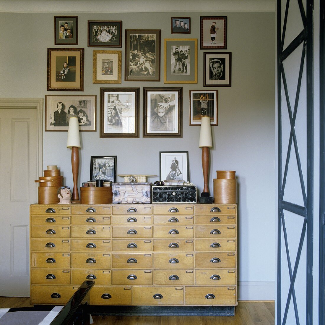 An old apothecary chest of drawers with a collection of photos hanging on the wall above it