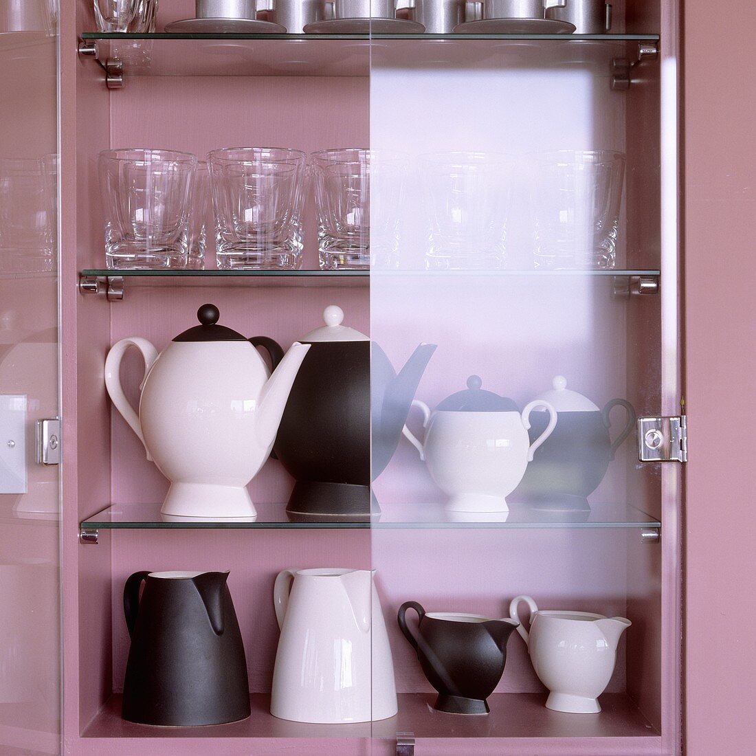 Black and white jugs, pots and glasses in a pink-painted cupboard with open glass doors