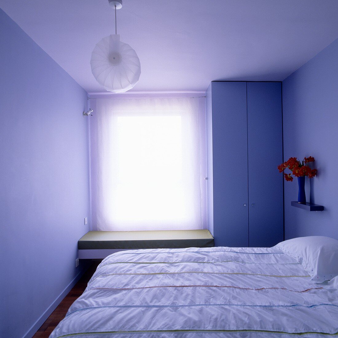 A small bedroom with a blind at the window and floor-to-ceiling wardrode