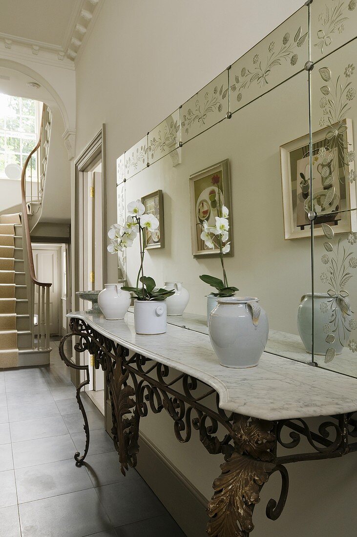A marble-topped, wrought iron side table and a mirror in a hallway of a town house