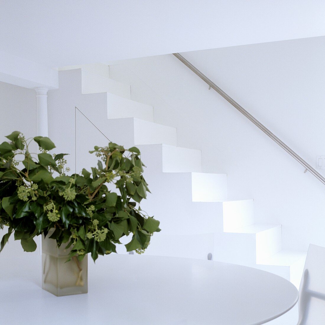 Weisser Raum mit Vase auf Tisch und Treppe mit Edelstahlhandlauf