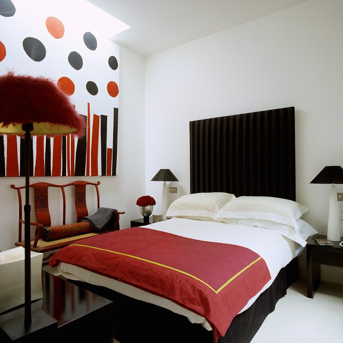 Rote Tagesdecke auf Bett mit schwarzem Kopfteil und Bild im weissen Schlafraum