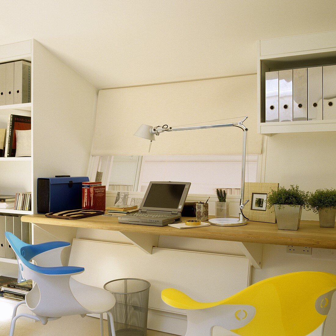 A desk with a wooden work surface mounted on wall brackets with coloured bucket chairs