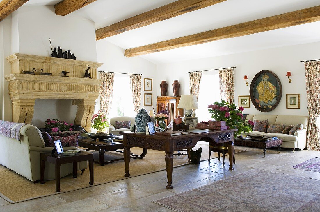 An antique desk and a sofa in front of a fireplace in a living room with a wood beam ceiling
