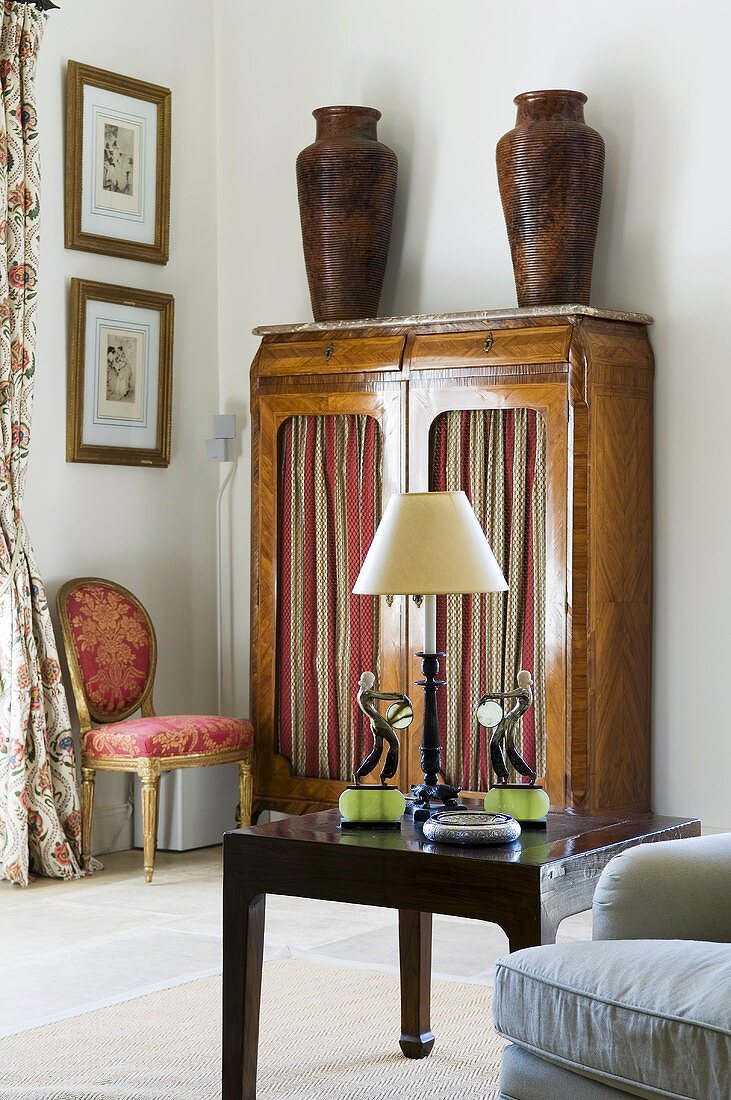 A corner of a room with a side table and vases on an antique cupboard