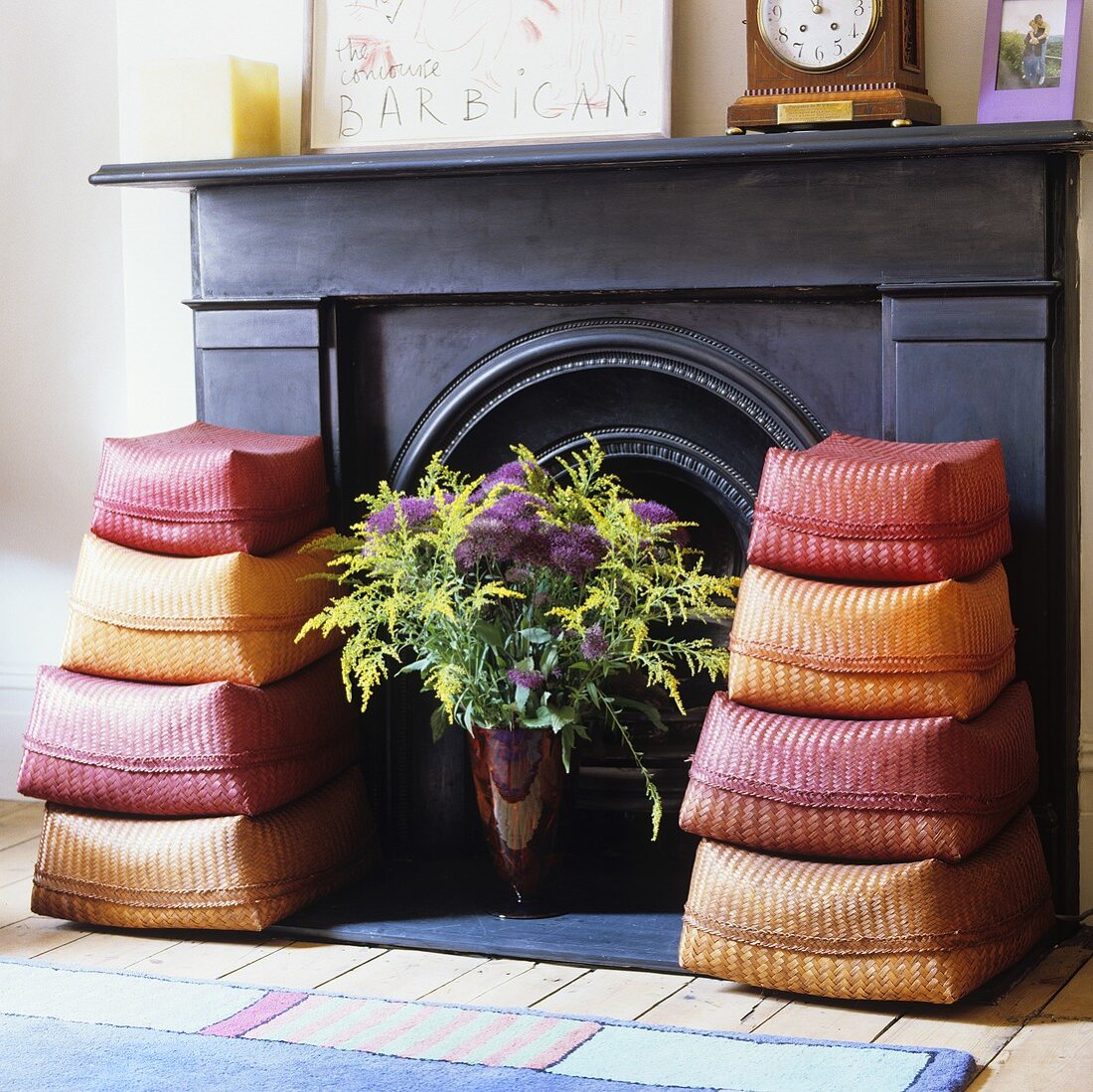 Two sets of colourful sisal baskets and a vase of flowers in front of a dark wood panelled fireplace