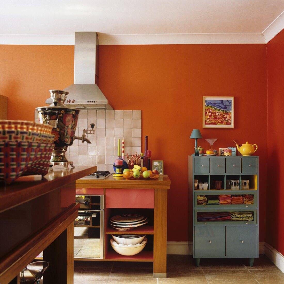 A kitchen in a country house with orange-painted walls and kitchen furnitures with a stainless steel extractor fan