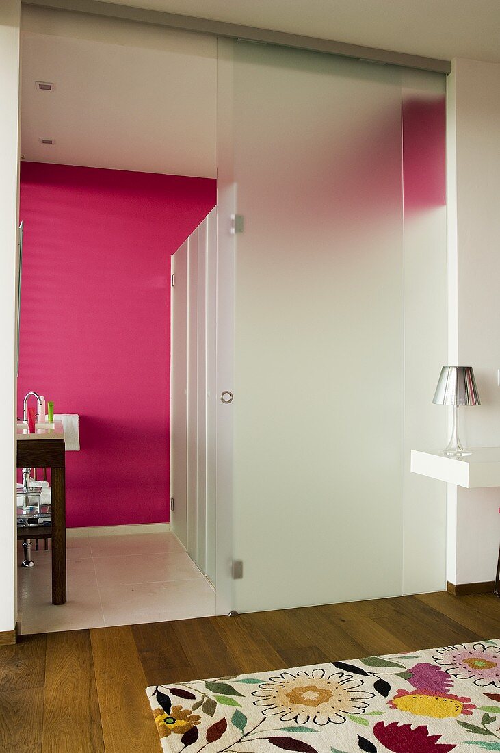 Opake Glaswand mit offener Schiebetür und pinkfarbene Wand im Bad