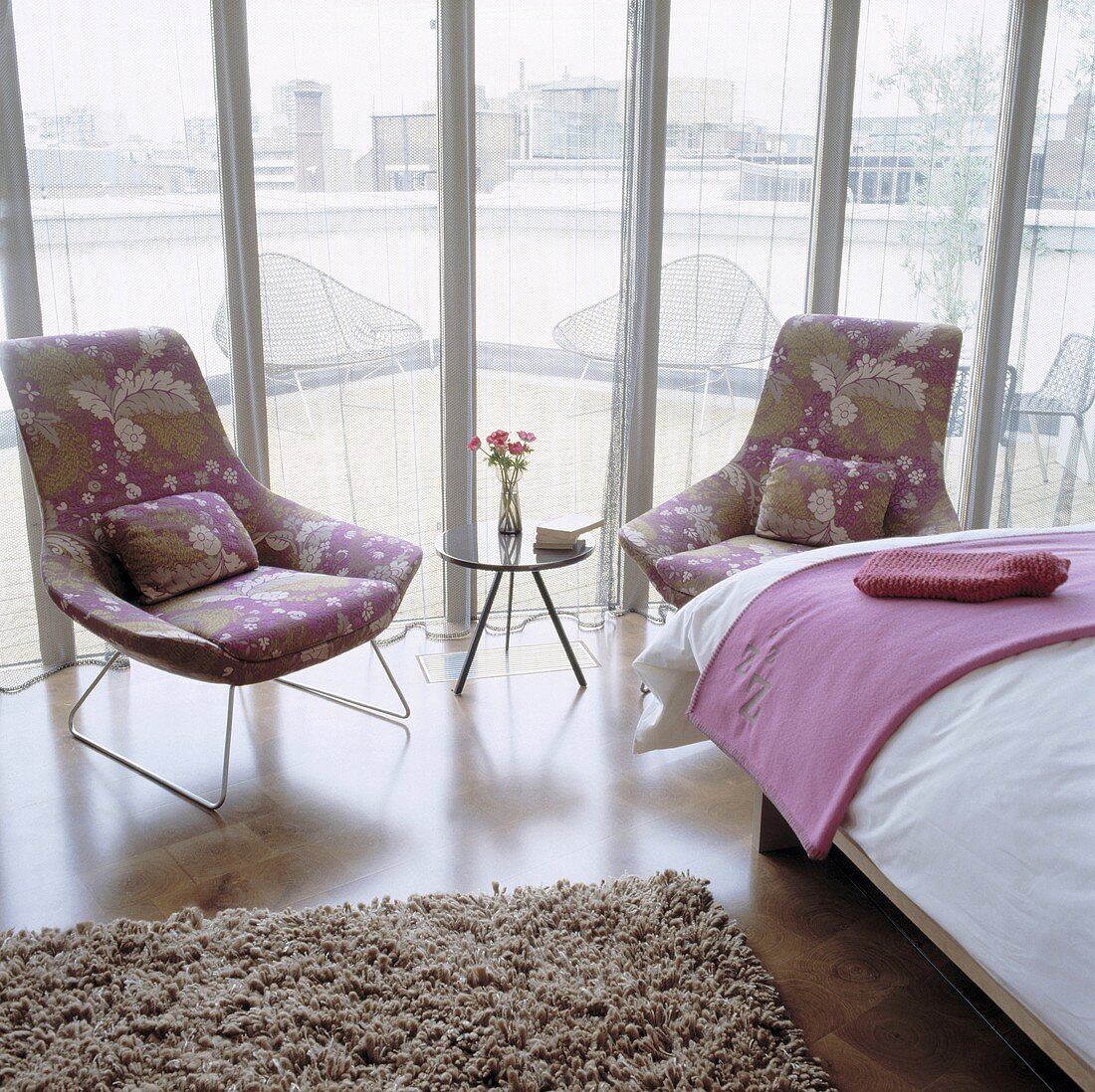 Floral patterned armchairs and a side table in front of a window with a transparent curtain