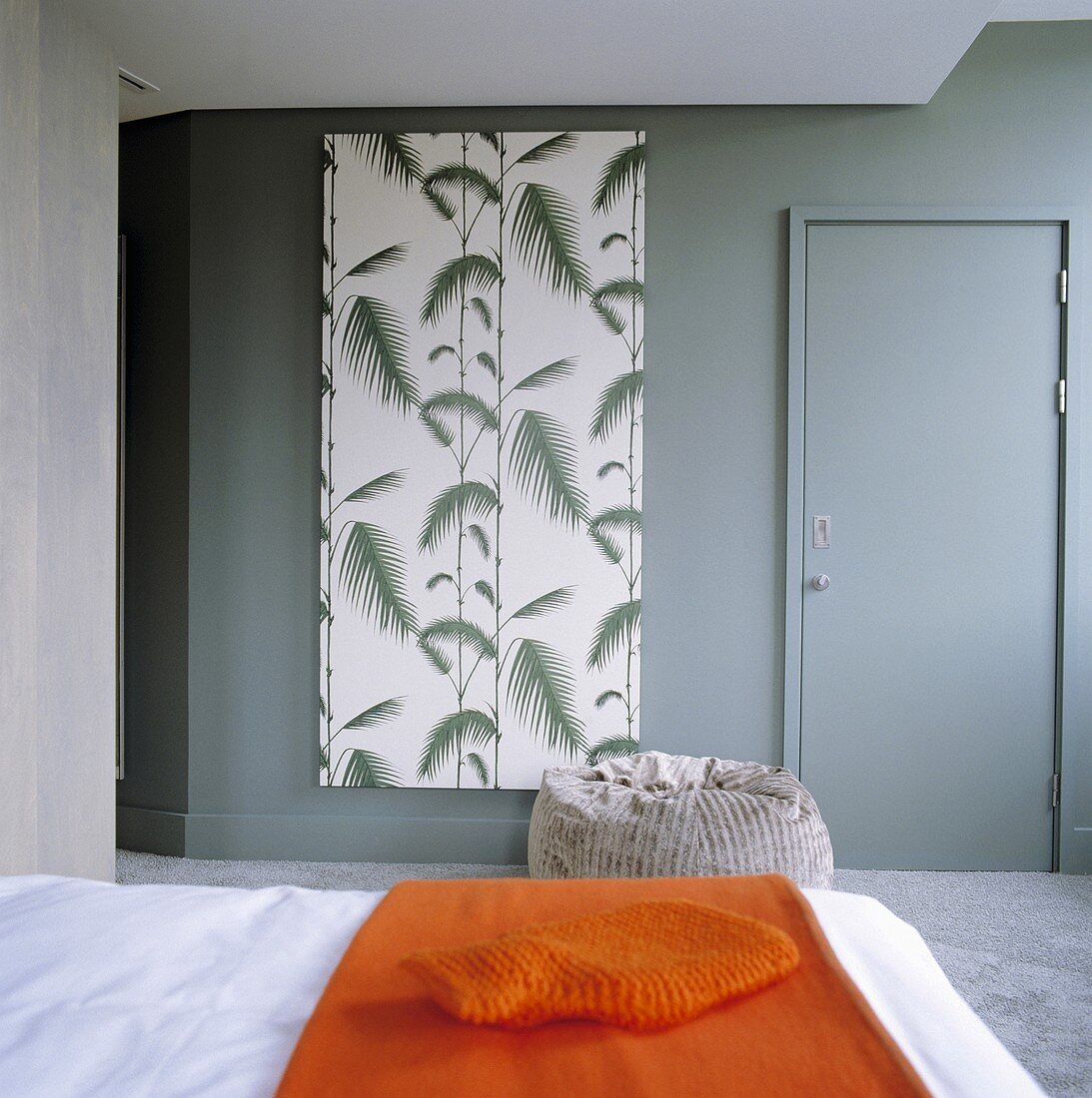 An orange quilt on a bed and a door in a grey wall