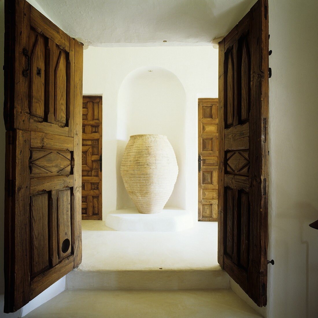 Blick durch offene Holzflügeltür auf Amphore in Wandnische eines Mediterraner Hauses