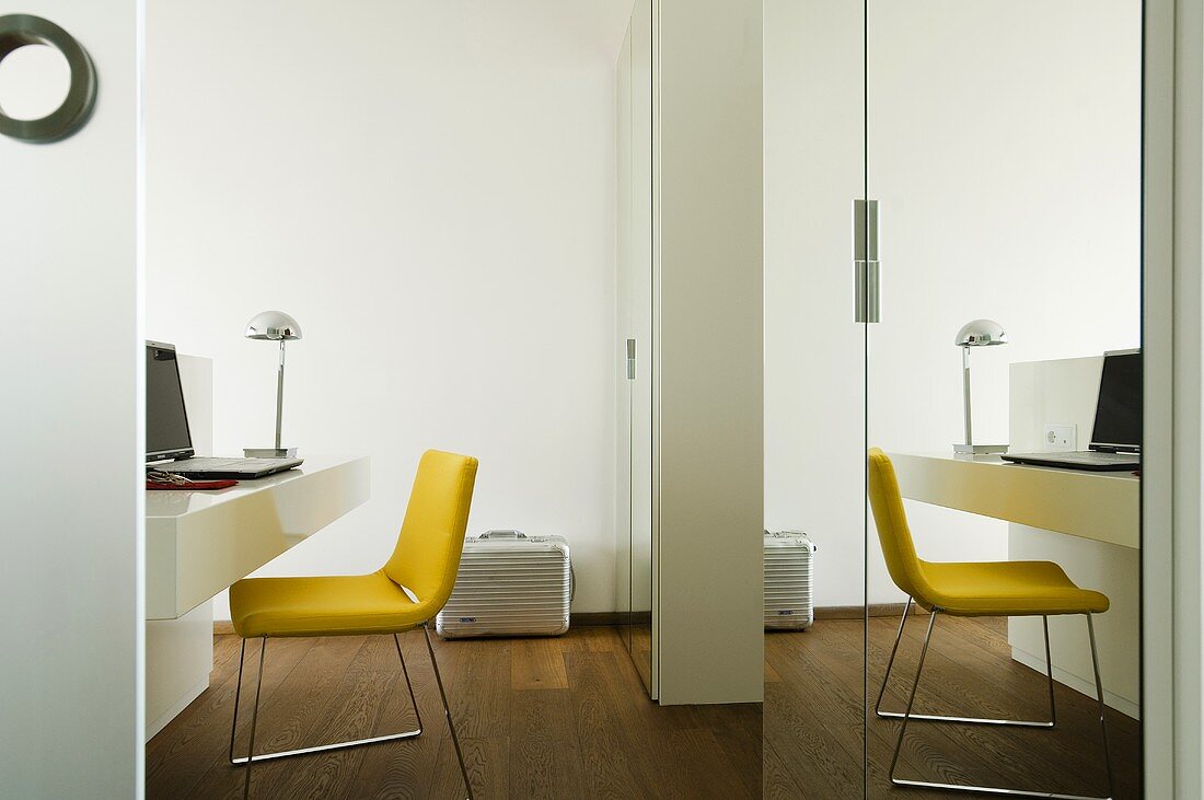 Arbeitstisch mit gelbem Polsterstuhl vor Spiegelschrank
