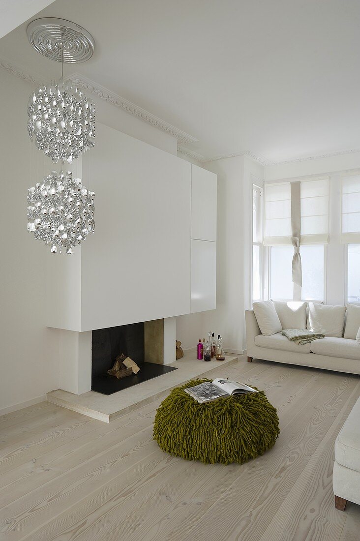 A minimalistic living room with a designer pendent lamp and a green floor cushion in front of a fireplace