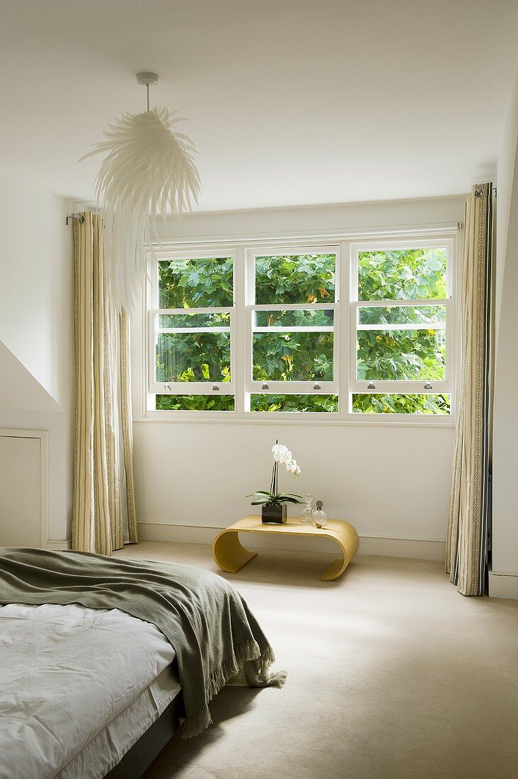 A bedroom - a curved side table under a window with a view of the garden