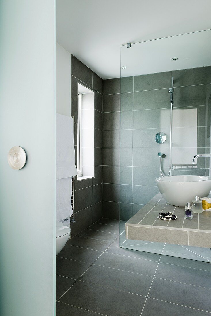 A grey tiled designer bathroom with a wash basin on a shelf
