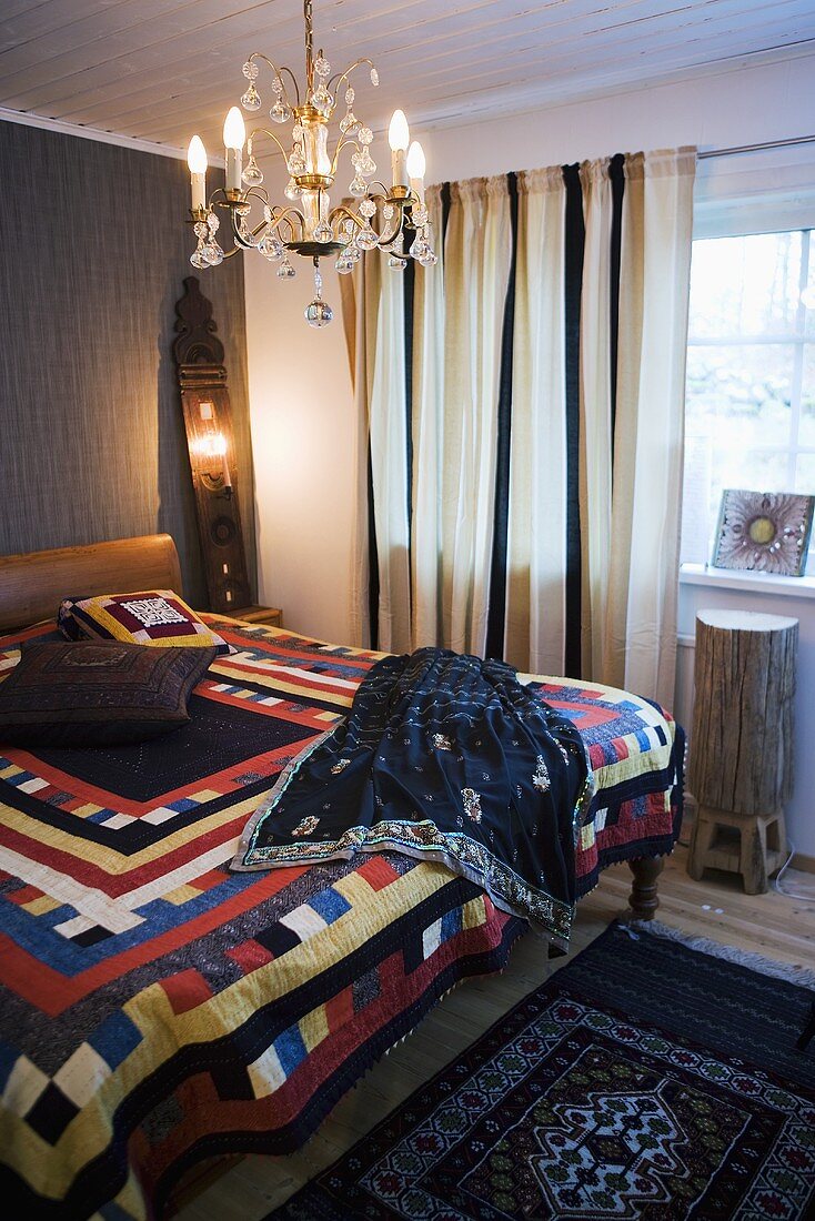 A bedroom - a bed with a colourful throw and a chandelier