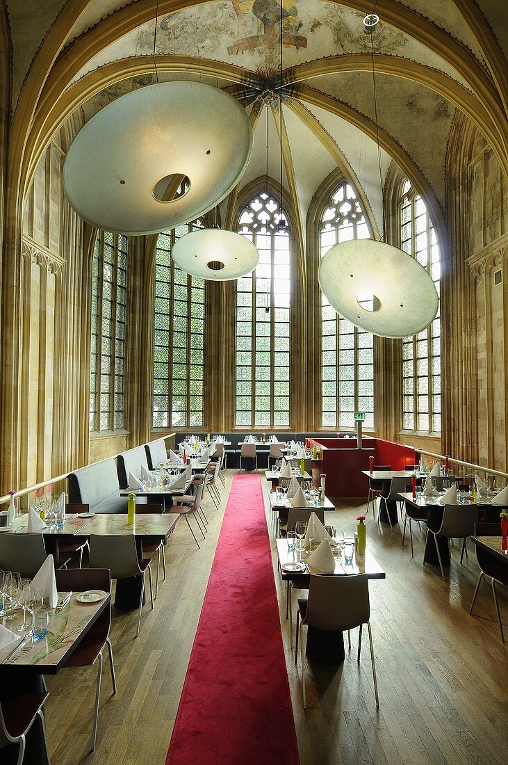 A designer restaurant in a converted church with a red carpet and extra large lampshades in the vaulted ceiling