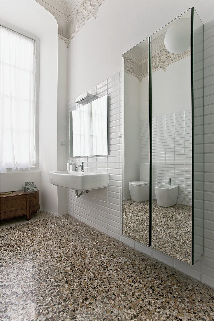 A stately bathroom with a terrazzo floor and a mirrored cupboard next to the wash basin