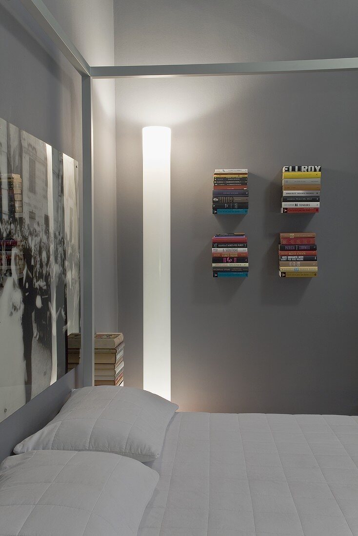 A corner of a bedroom - an illuminated designer floor lamp and minimalistic shelves on a grey wall